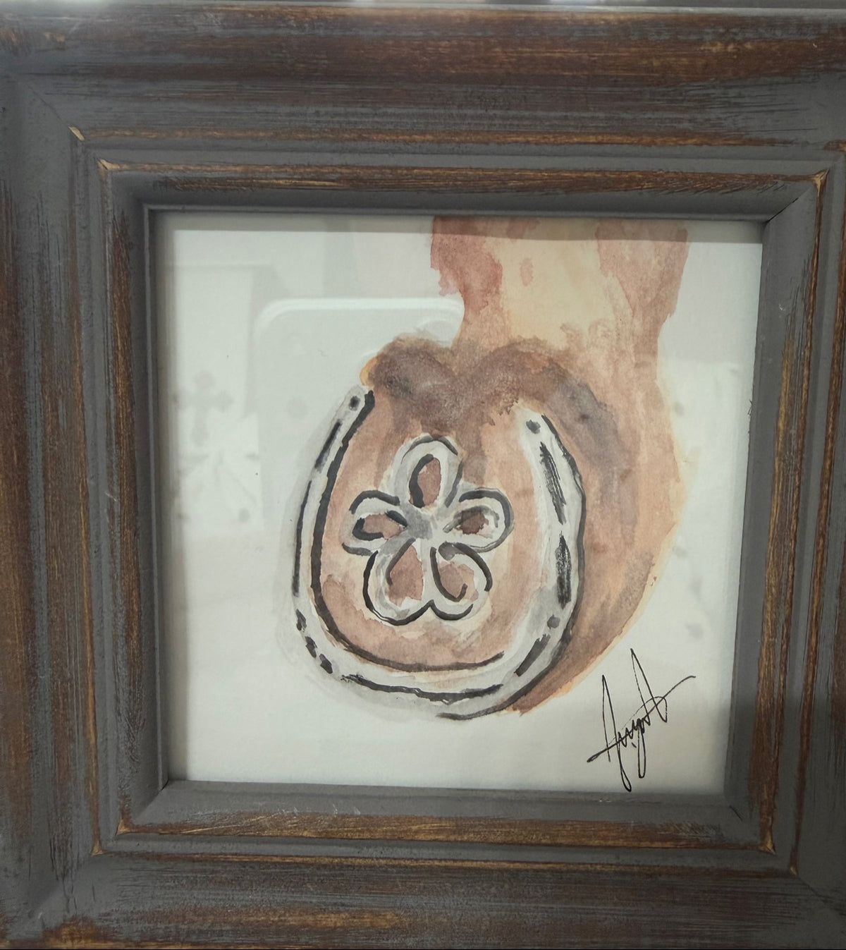 Inspired watercolor painting of a horseshoe with a flower at its center, in warm sepia tones, by Selena Angeles, framed in distressed dark wood