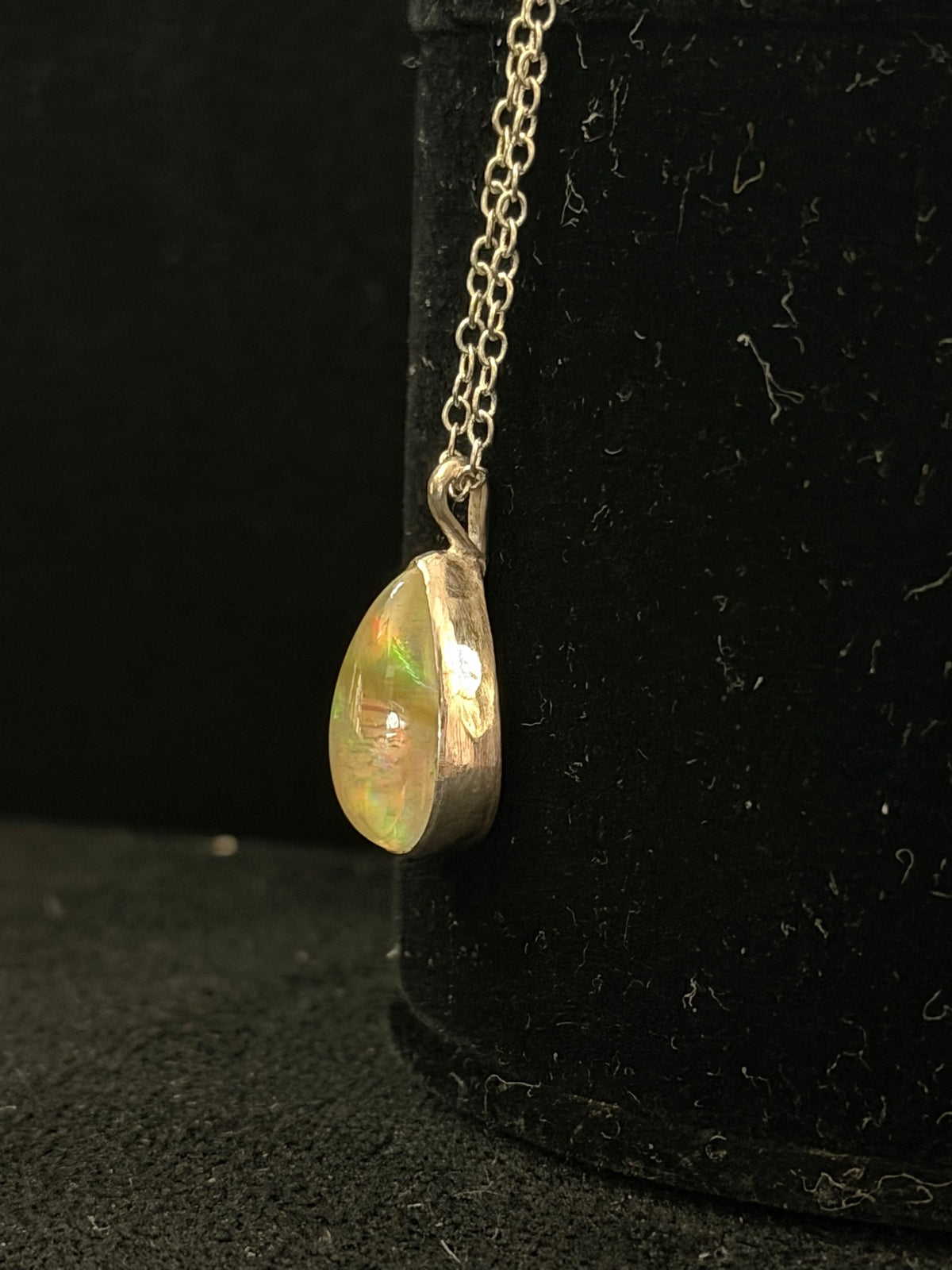 Side view of the DM6 Ethiopian opal teardrop pendant showing the deep sterling bezel and the opal's fire