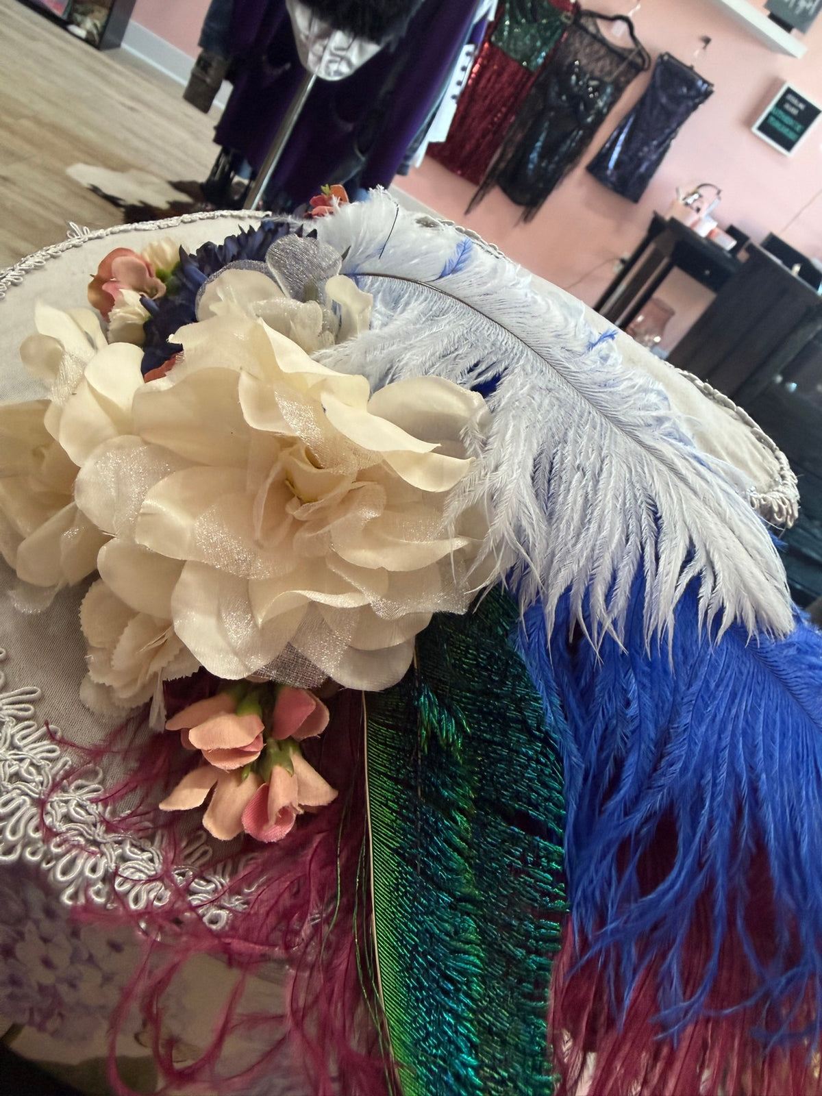 Close-up detail of Miss Crosby's vintage gray wide-brim hat — cream silk roses, white and royal blue ostrich plumes, peacock feather and lace trim