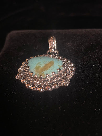 Genuine turquoise pendant - angled front view of the pale oval stone and its scallop bezel, stone forward on black