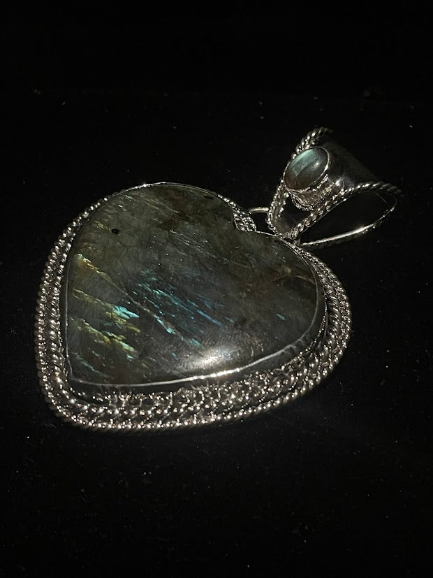 Labradorite heart pendant - angled view of the heart and its wide bail with a small pale cabochon, on black