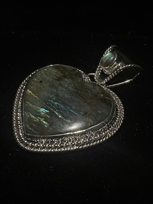 Labradorite heart pendant - angled view of the heart and its wide bail with a small pale cabochon, on black