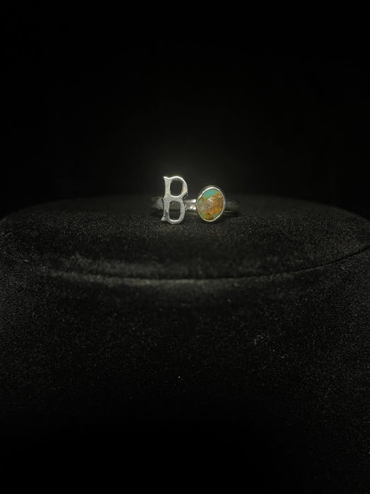 Turquoise initial ring — letter B in sterling silver beside a round stone with golden matrix, on black