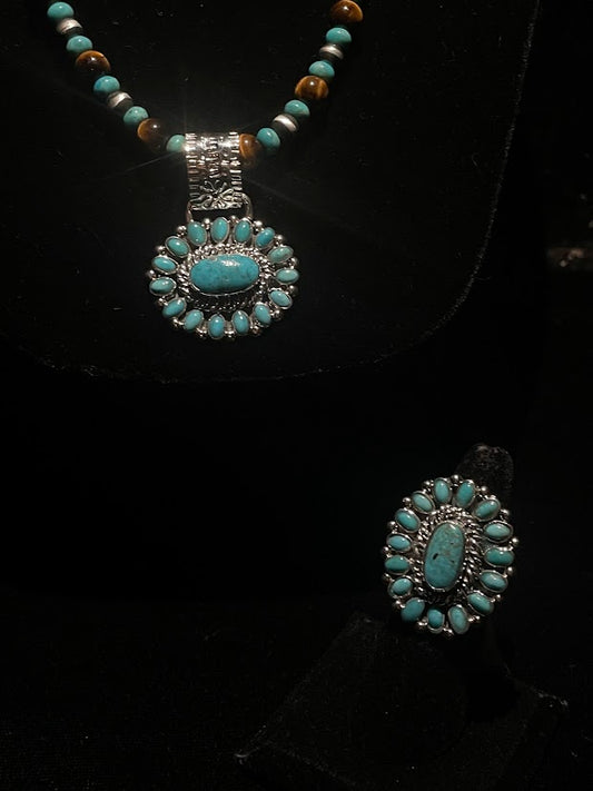 Turquoise ring — the ring standing front-on below a matching turquoise cluster pendant on a beaded necklace, on black velvet