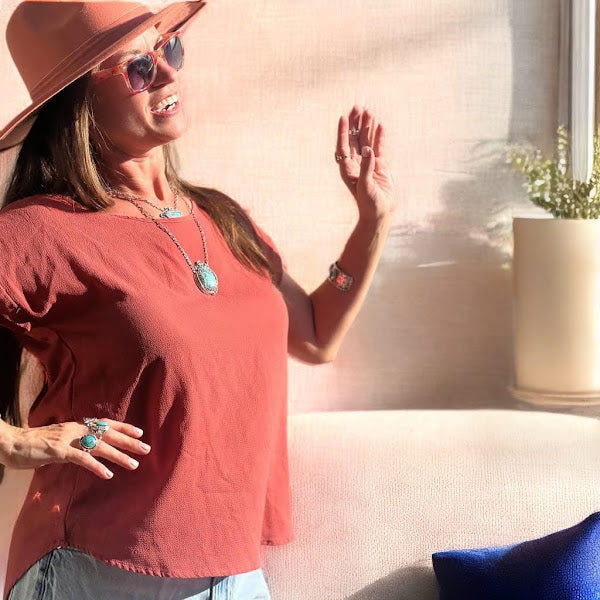 Turquoise ring — a smiling woman in a tan hat and sunglasses wears a full turquoise jewelry look outdoors, rings among it