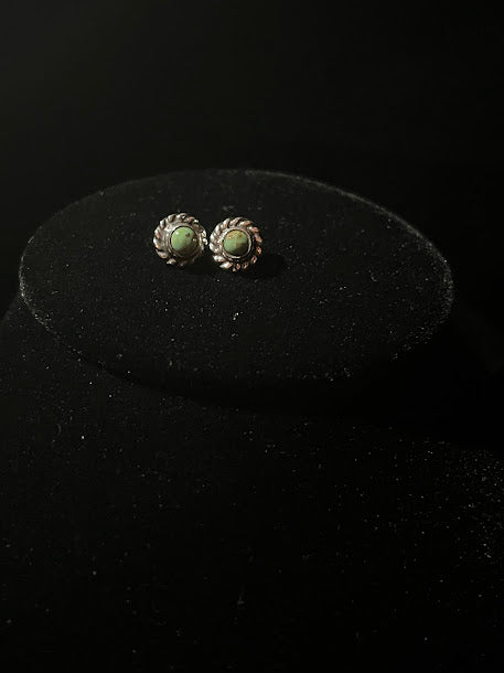 Turquoise stud earrings — the mini pair face up on a black oval stand, green cabochons in rope bezels