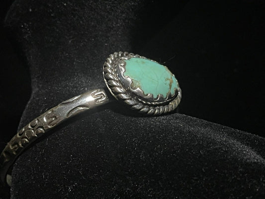 Turquoise cuff bracelet — oval turquoise stone in a rope bezel with the stamped sterling band, side view on black