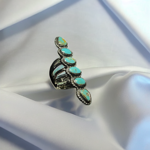 Turquoise ring — the long six-stone row resting on white satin, spiral band and rope bezels showing from the side