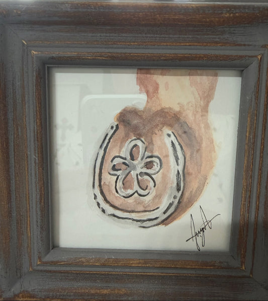 Inspired watercolor painting of a horseshoe with a flower at its center, in warm sepia tones, by Selena Angeles, framed in distressed dark wood