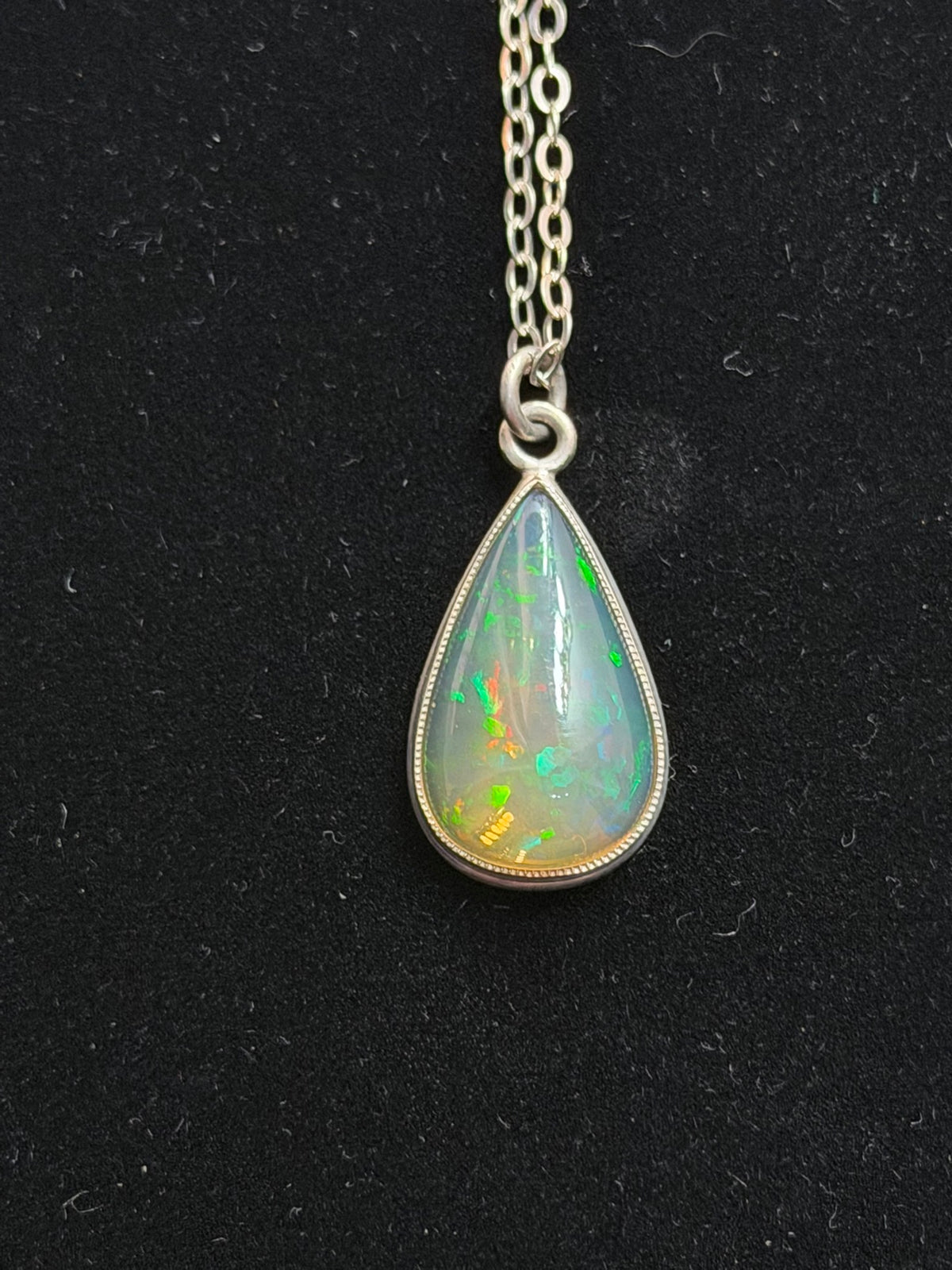 DM7 Ethiopian opal teardrop pendant necklace on black, showing green and orange fire