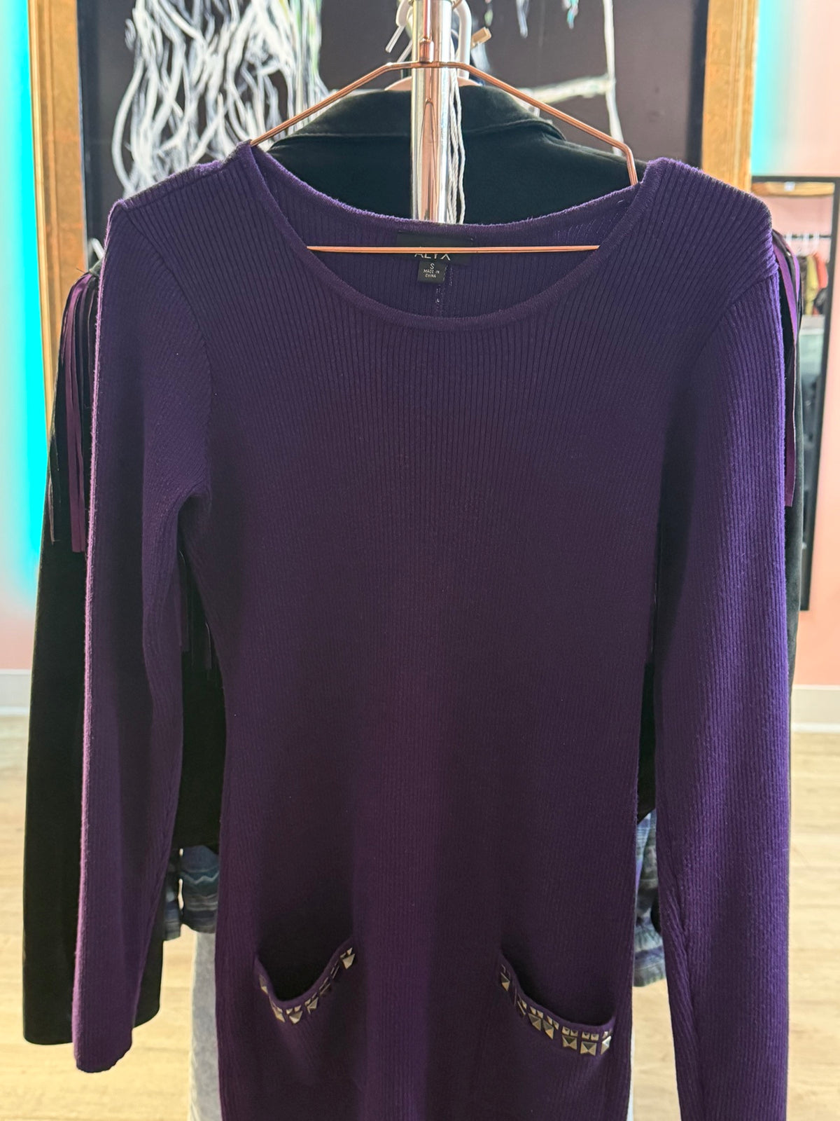 Front view of an ALYX purple long-sleeve ribbed sweater dress with front patch pockets hanging on a copper hanger.