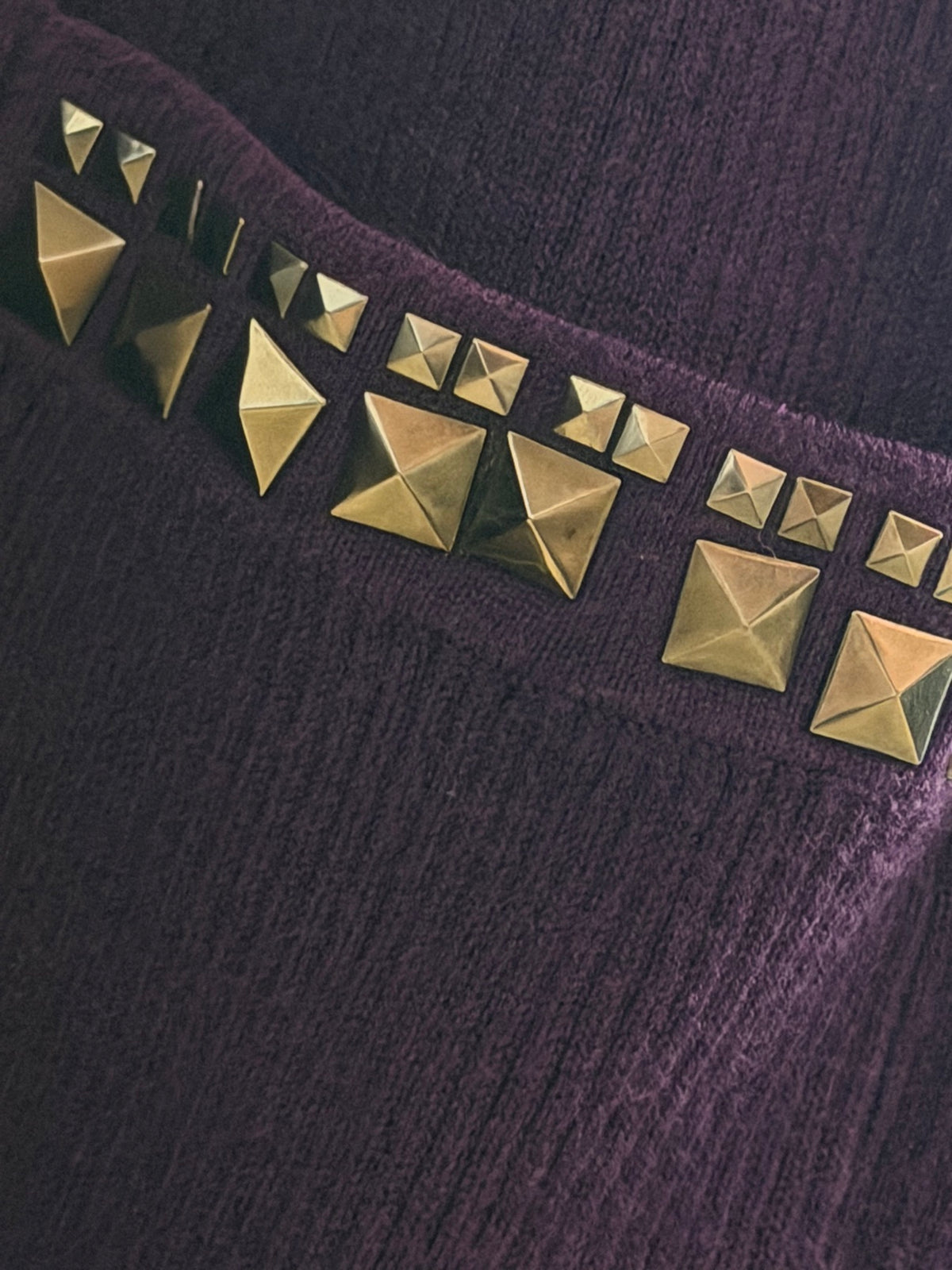 Close-up of the metallic studded trim detailing on the front pocket of a deep purple knit dress.