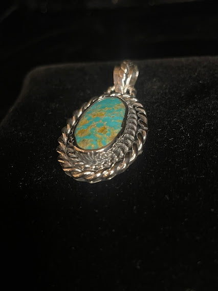 Genuine turquoise pendant - angled front view of the tall oval stone and its rope bail, stone face forward on black