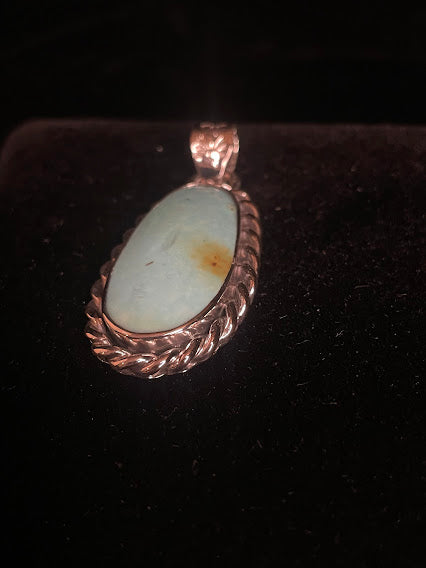 Genuine turquoise pendant - angled front view of the tall oval stone and its flower sunset bail, face forward on black