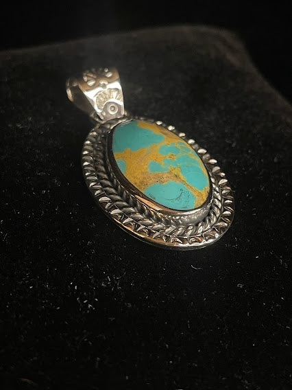 Genuine turquoise pendant - angled front view of the turquoise-blue oval stone and its stamped sunset bail, stone forward