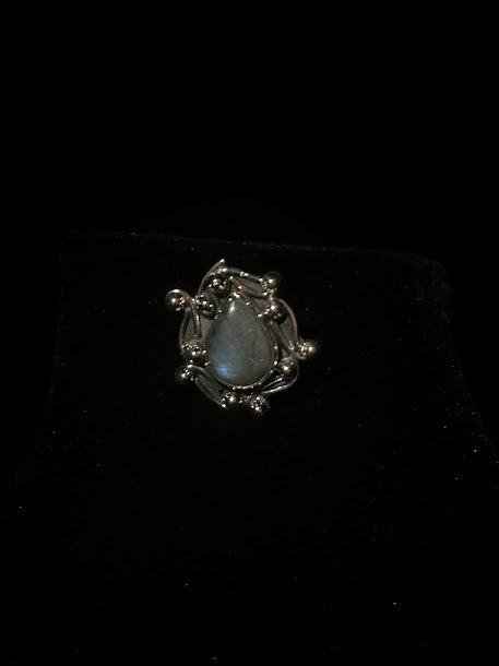 Labradorite teardrop ring — gray teardrop stone with a blue flash in a silver ball and swirl frame, on black velvet