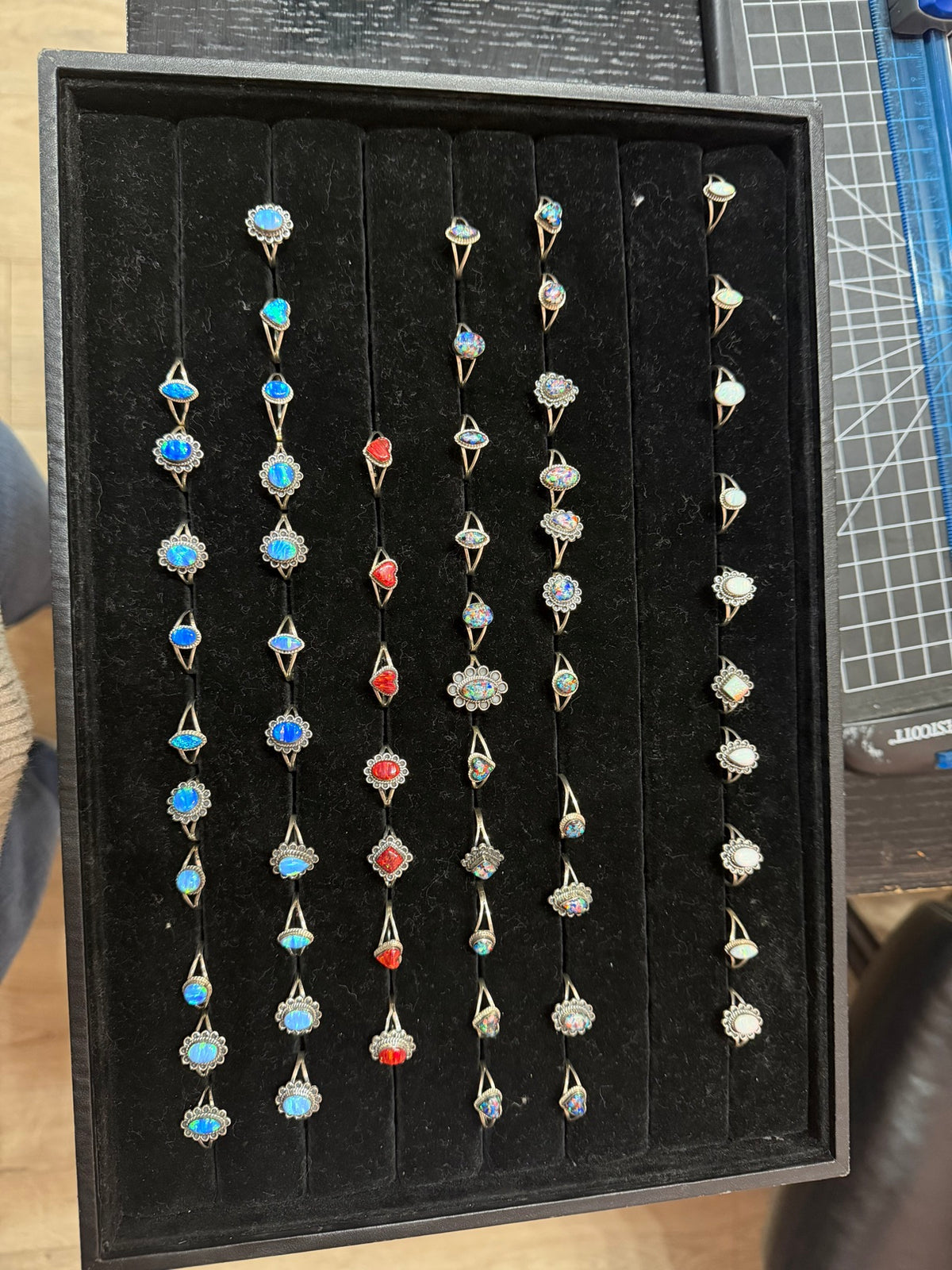 Opalite ring — a black tray of sterling silver opalite rings in light blue, red, kaleidoscope and white