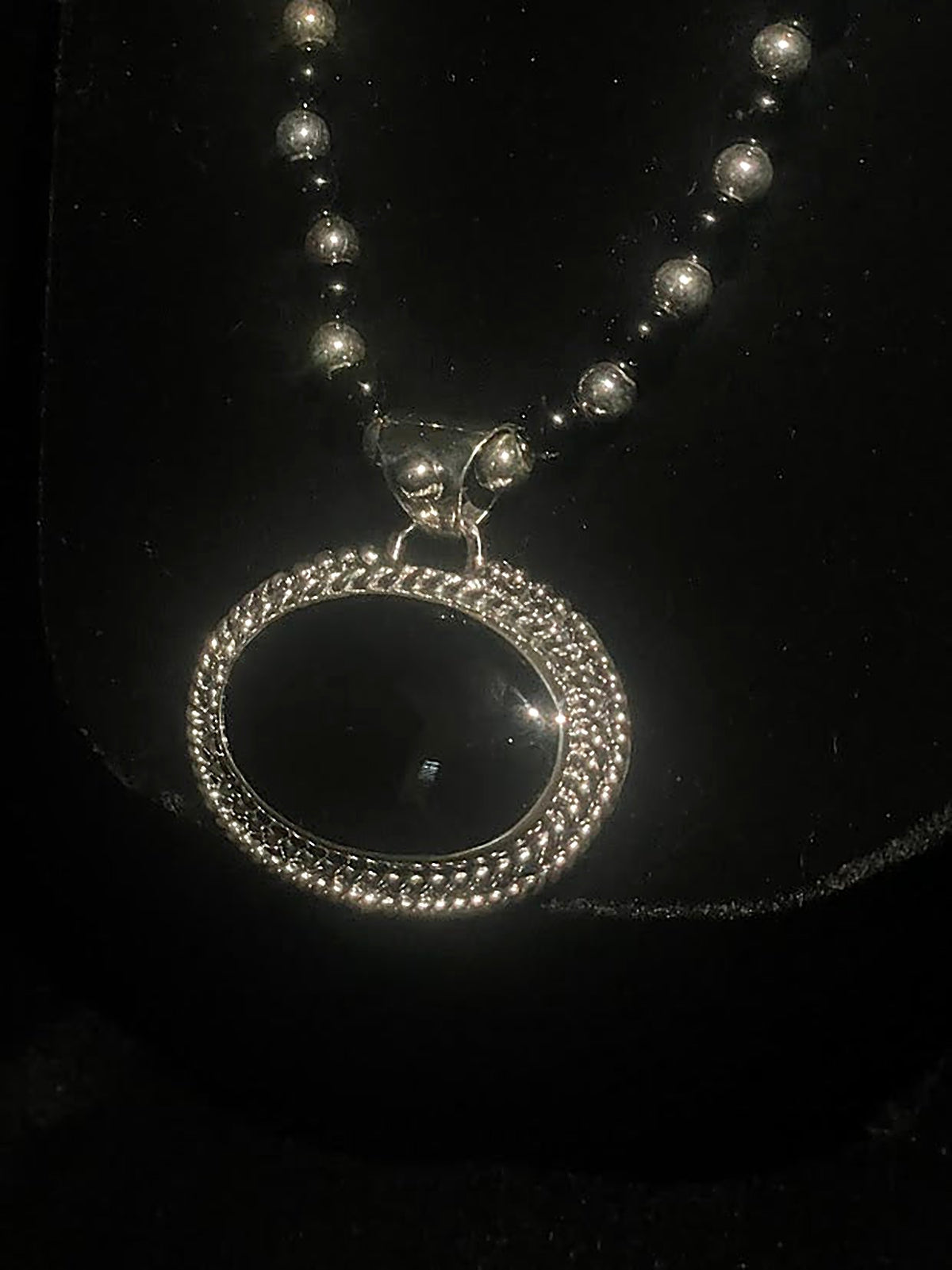 Oval obsidian pendant — close front view of the black oval stone in its sterling silver beaded frame on black