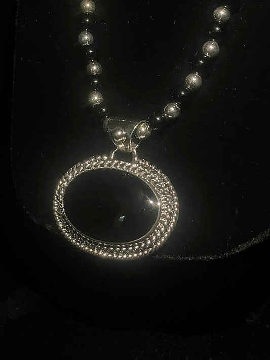 Oval obsidian pendant — close front view of the black oval stone in its sterling silver beaded frame on black