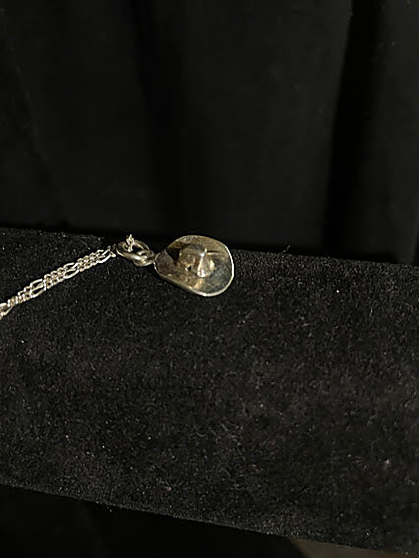 Sterling silver cowboy hat pendant — close view of the polished silver hat, its raised crown and bail, on black