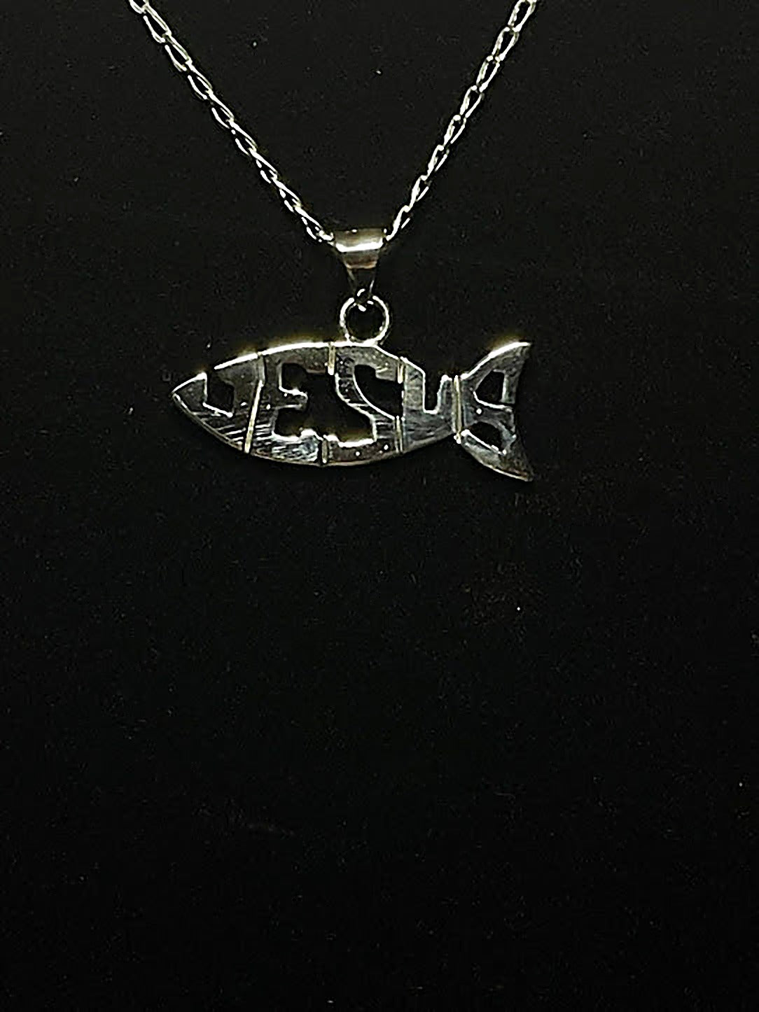 Sterling silver Jesus fish pendant, the name JESUS cut clean through the fish, hanging on its fine chain on black