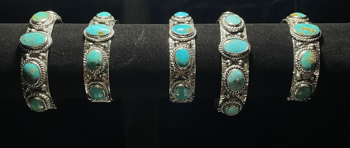Turquoise cuff — five sterling silver cuffs with oval turquoise stones standing in a row on a black display bar