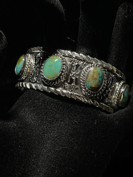 Turquoise cuff — four oval turquoise stones across a textured sterling band, full view on a black display