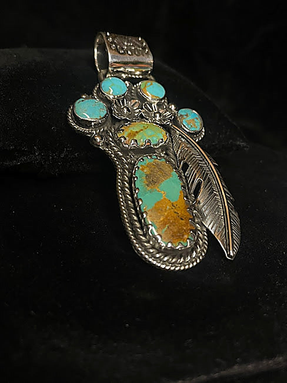 Turquoise feather pendant — front view of its six turquoise stones and the silver feather, on black velvet