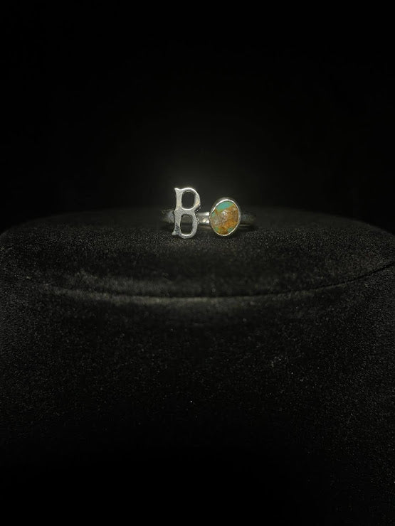 Turquoise initial ring — letter B in sterling silver beside a round stone with golden matrix, on black