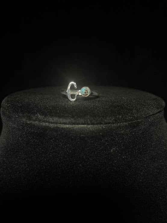 Turquoise initial ring — letter C in sterling silver beside a small round blue stone, on black velvet