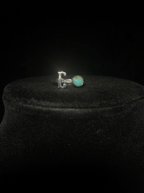 Turquoise initial ring — letter E in sterling silver beside a round bright blue stone, on black velvet