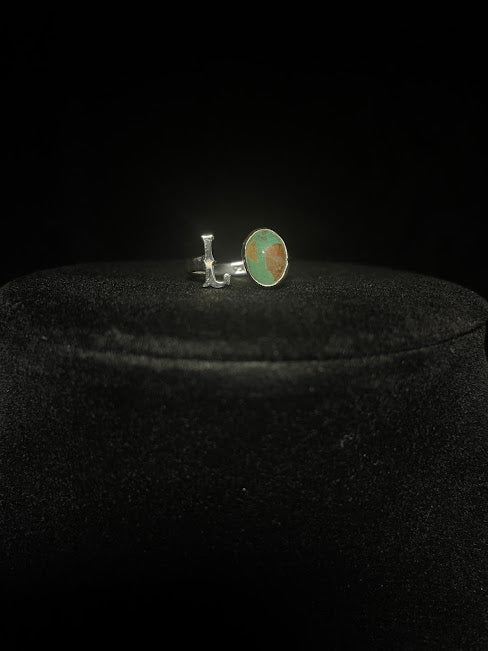 Turquoise initial ring — letter L in sterling silver beside an oval green-blue stone, on black velvet