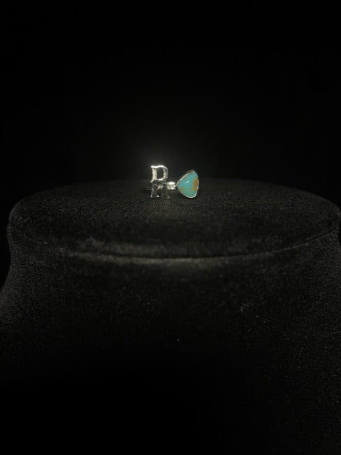 Turquoise initial ring — letter R in sterling silver beside a blue teardrop stone, another R ring, on black