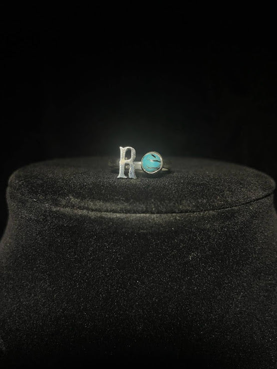 Turquoise initial ring — letter R in sterling silver beside a round blue stone with dark matrix, on black