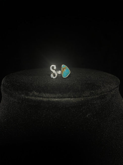 Turquoise initial ring — letter S in sterling silver beside a blue triangular stone with brown matrix, on black