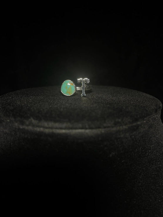 Turquoise initial ring — letter T in sterling silver beside a green teardrop stone, on black velvet