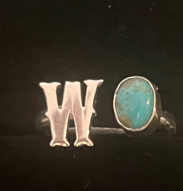 Turquoise initial ring — letter W in sterling silver beside an oval blue stone, close view on black