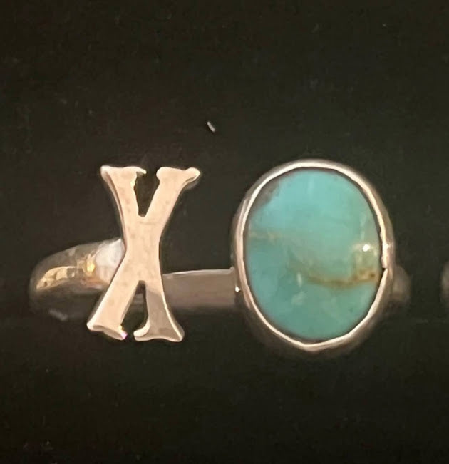 Turquoise initial ring — letter X in sterling silver beside an oval blue stone, close view on black
