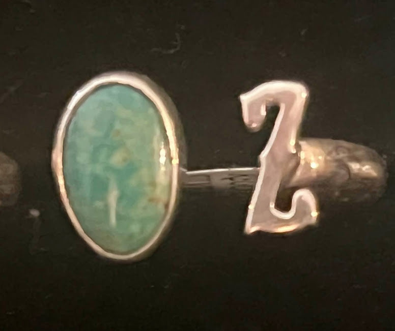 Turquoise initial ring — letter Z in sterling silver beside an oval green stone, close view on black