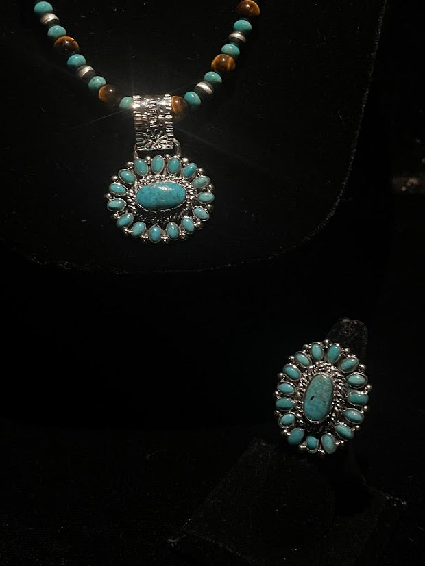 Turquoise ring — the ring standing front-on below a matching turquoise cluster pendant on a beaded necklace, on black velvet