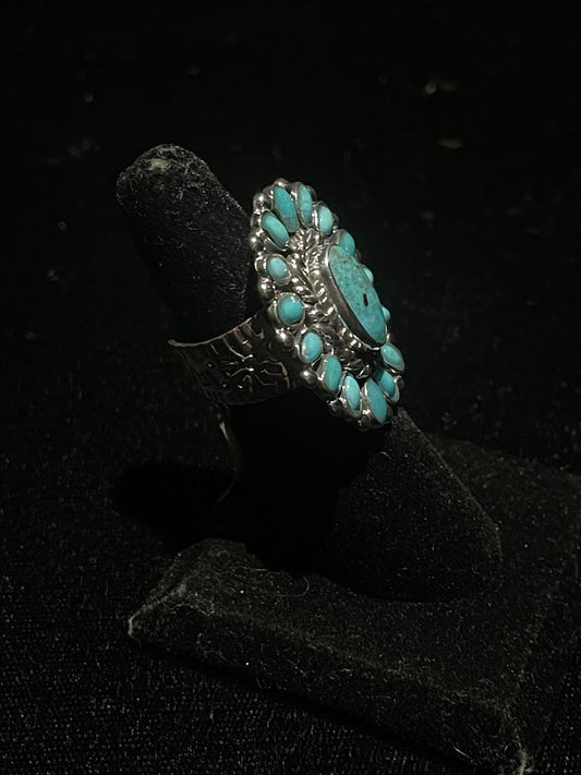 Turquoise ring — side view of the oval halo cluster face and stamped sterling silver band, on a black velvet stand