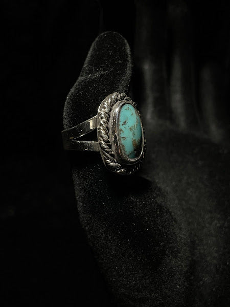 Turquoise ring — side profile on black velvet, the oval stone edge and rope bezel above the split shank band