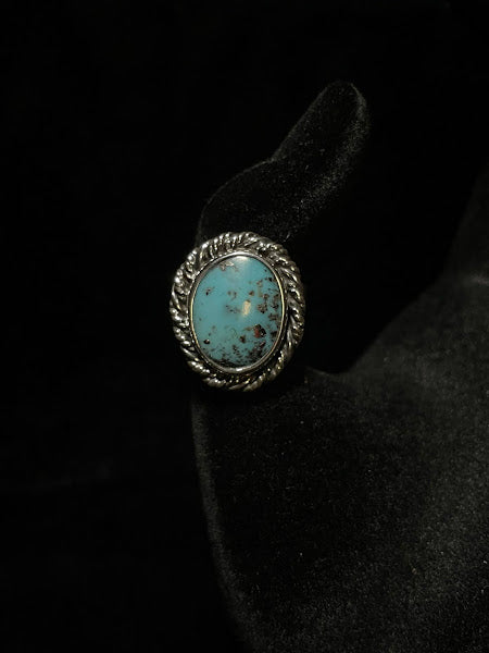 Turquoise ring — front view of the pale blue oval stone with fine dark speckling inside its rope bezel, on black velvet