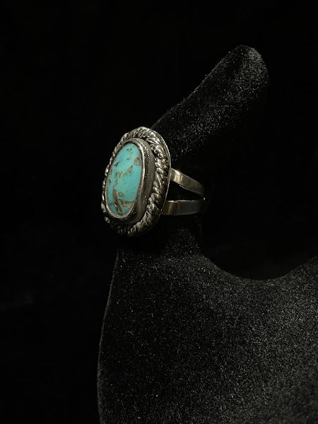 Turquoise ring — angled view of the greener oval stone in its rope bezel on a black velvet hand form