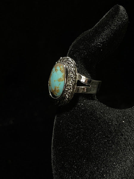 Turquoise ring — angled view of the blue-green oval stone with brown matrix low on its face, rope bezel, black velvet