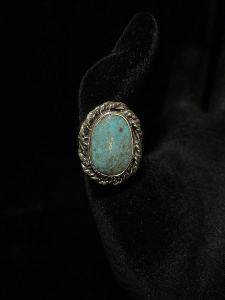 Turquoise ring — front view of the oval stone carrying golden-brown matrix across blue-green, rope bezel, on black velvet
