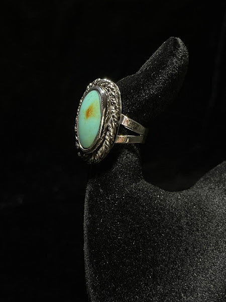 Turquoise ring — side view of the pale mint oval stone with one amber spot, rope bezel, on black velvet