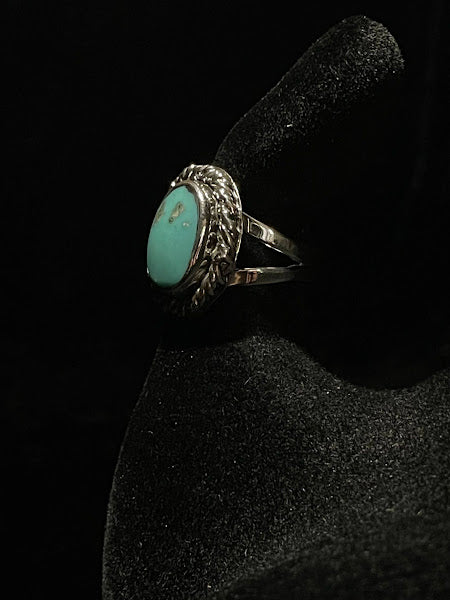 Turquoise ring — angled view of the smooth green oval stone with faint marks, rope bezel, on black velvet