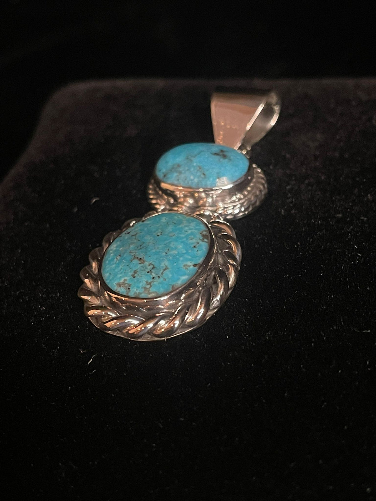 Two-stone turquoise pendant — angled close view of vivid blue stones and twisted rope silverwork, on black