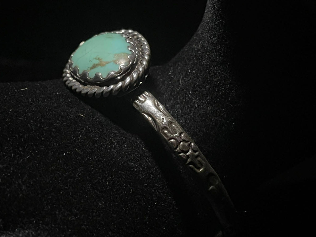 Turquoise cuff bracelet — angled view of the turquoise stone, rope bezel, and stamped band on a black display
